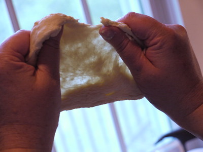 Baker holds bread dough to the light, stretching for window-pane test.